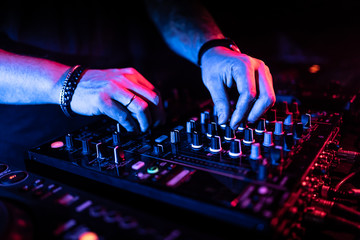 Close up of DJ hands controlling a music table in a night club.