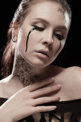 portrait of young brunette girl with black tears from eyes and lace pattern on face and neck posing...