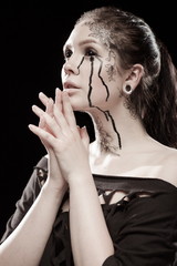 portrait of young brunette girl with black tears from eyes and lace pattern on face and neck posing...