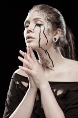 portrait of young brunette girl with black tears from eyes and lace pattern on face and neck posing...