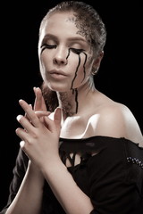 portrait of young brunette girl with black tears from eyes and lace pattern on face and neck posing...