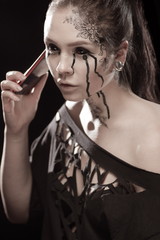 portrait of young brunette girl with black tears from eyes and lace pattern on face and neck posing...