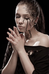 portrait of young brunette girl with black tears from eyes and lace pattern on face and neck posing...