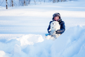 Fototapeta na wymiar A boy with a white dog Spitz walks in winter in the snow