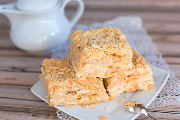 Baked tasty pieces of creamy cake on white plate and wooden table. Sugar dessert concept