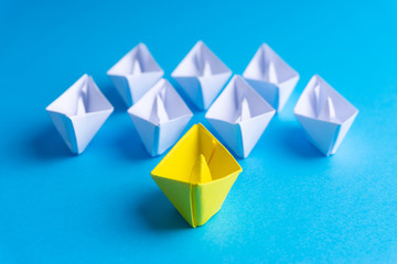 White and yellow paper boat or ship in one direction on blue background. Business for innovative...
