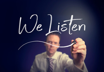 A businessman writing a We Listen concept with a white pen on a clear screen.
