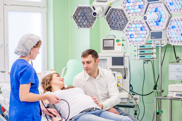 Beautiful pregnant woman with her husband in medical clinic. Nurse measuring pressure of pregnant woman