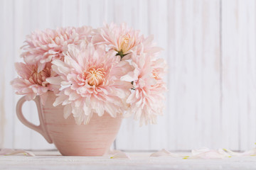 chrysanthemum in pink cup on white wooden background