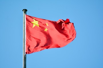 Chinese flag with flag pole waving in the wind over blue sky background