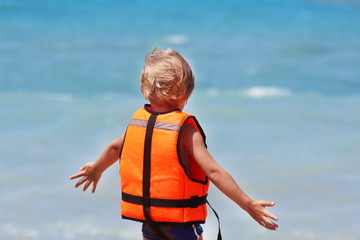 Safety of life concept. Little caucasian boy uses a life jacket on a summer beach against the...