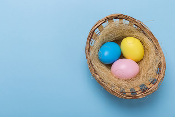 Colorfull easter eggs in nest on blue pastel color background with space.