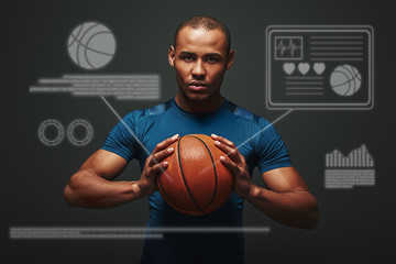 Ready to play. Handsome sportsman standing over dark background holding basketball ball in his hands. Game concept with graphic drawing.