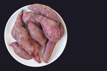 Close-up Of Fresh purple yams pile on white dish with black background.