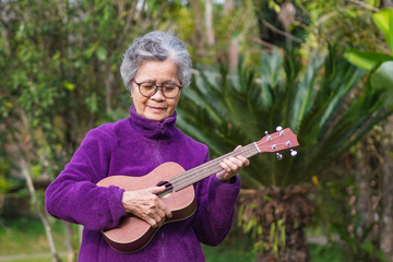 Portrait of elderly woman playing ukulele in her garden.