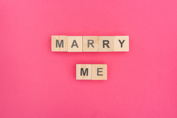 top view of marry me lettering made of wooden cubes on pink background