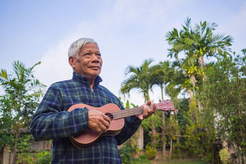 Portrait of senior man playing ukulele in his garden.