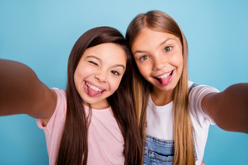 Close up photo two pretty little age girls holiday having fun funky childish glad tongue out of mouth make take selfies wearing casual jeans denim t-shirts isolated on blue bright background