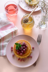 Stack of pancakes with frozen raspberry, red currant and honey on pink background. Selective focus