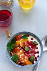 Bowl of homemade granola with yogurt, citrus and pomegranate seeds on gray wooden background. Selective focus. Healthy eating or vegetarian food concept