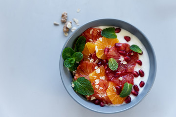 Bowl of homemade granola with yogurt, citrus and pomegranate seeds on gray wooden background....