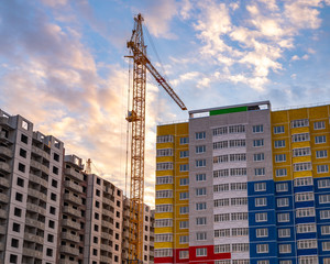 crane and building under construction. Construction crane and bright colored high-rise building on the background of a beautiful cloudy evening sky