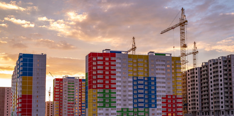 crane and building under construction. Construction crane and bright colored high-rise building on the background of a beautiful cloudy evening sky
