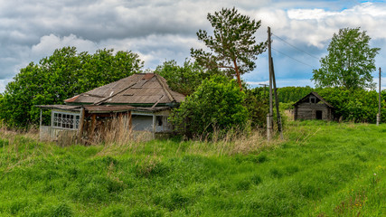 Old crashed wooden house in an abandoned village on a cloudy sky background. The ruins of a wooden hut on a grassy street