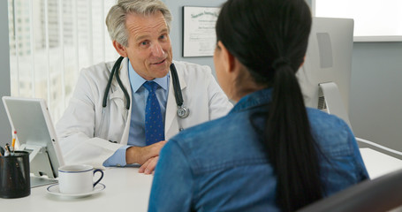 Fototapeta premium High angle view of senior Caucasian male doctor in his office talking to new patient and smiling. Primary care physician explaining medical issue to woman