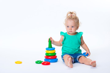 Obraz premium Cute kid blonde girl playing with color pyramid toy isolated on white background. Happy childhood and pre-school development of children