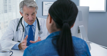 Medical doctor talking to female patient at desk. Physician explaining health care options to woman in his office