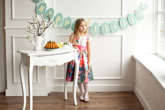 Full length of a little smiling girl in colorful dress posing in a decorated room for the holiday Easter is waiting for an Easter lunch