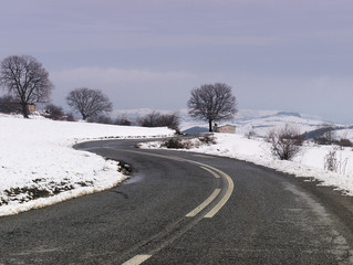 Road leading to a Distant bare tree and an old building on snow covered land