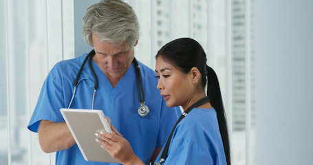 Two friendly medical professionals working together on tablet computer. Medium shot of Japanese woman doctor and Caucasian male nurse going over digital paperwork in hospital