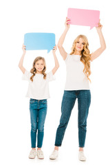 Obraz premium beautiful woman with adorable daughter holding speech bubbles in raised hands isolated on white