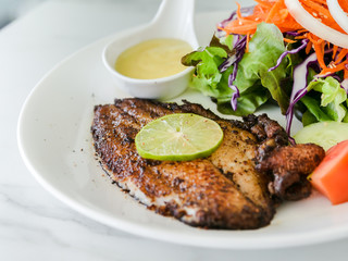 Grilled fish steak with salad with white plate on marble table.
