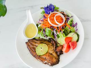 Grilled fish steak with salad with white plate on marble table.