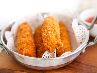 Fried cheese sticks in aluminium pan on wooden table, ready to eat.