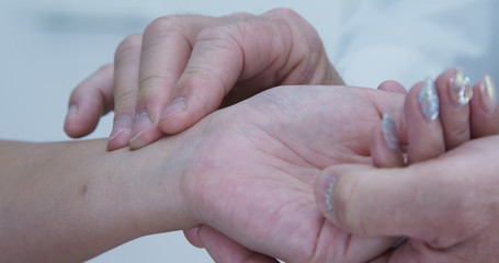 Extreme close-up on hands of doctor taking radial pulse on wrist of female patient. Woman with bedazzled nail art having heart rate measured by medical professional