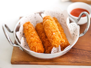 Fried cheese sticks in aluminium pan on wooden table, ready to eat.