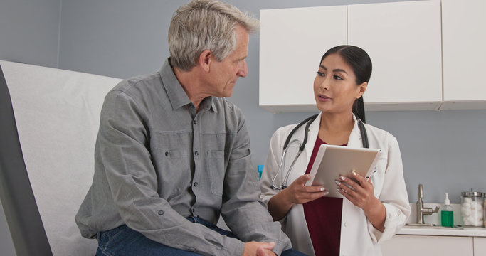 Primary care doctor explaining medical issue to senior male patient in exam room. Female medical professional with tablet computer talking to older man about his health
