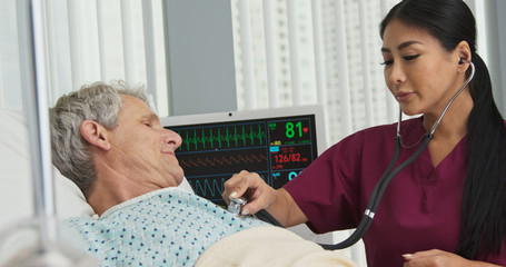 Doctor listening to breathing of man in hospital bed with stethoscope. Senior Caucasian man...
