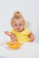 Cute little baby girl 1 year old in yellow t-shirt eating cereal flakes at the table isolated on...