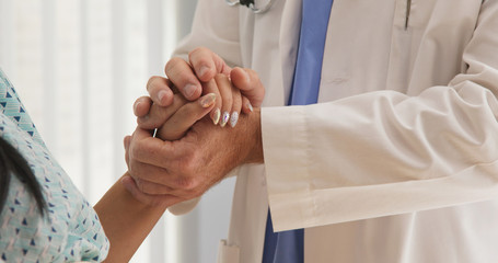 Sympathetic older doctor holding hands of female patient giving support. Supportive and caring male medical professional with woman patient. Close up on hand