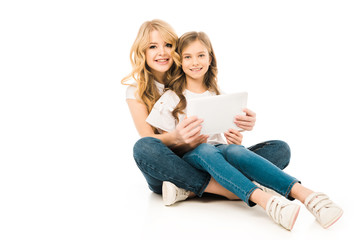 pretty woman and cute child using laptop while sitting on floor and looking at camera on white background