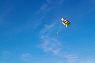 Naklejka na ściany i meble Parasailing water amusement. Flying on a parachute behind a boat on a summer holiday by the sea in the resort. Beautiful bright blue sky and colorful parachute.