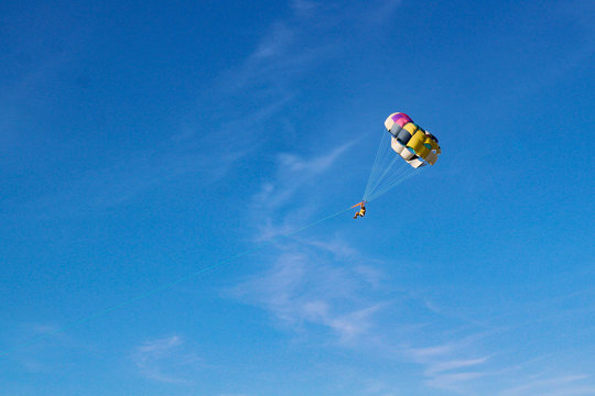 Parasailing water amusement. Flying on a parachute behind a boat on a summer holiday by the sea in the resort. Beautiful bright blue sky and colorful parachute.