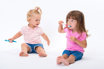 Two girls sisters in pink t-shirt with toothbrushes stand to their full height isolated on white background. Children oral and dental hygiene