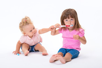Two girls sisters in pink t-shirt with toothbrushes stand to their full height isolated on white background. Children oral and dental hygiene