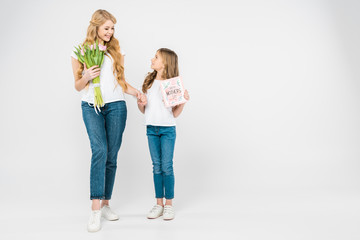 happy mother with beautiful pink tulips, and smiling daughter with happy mothers day greeting card holding hands on white background